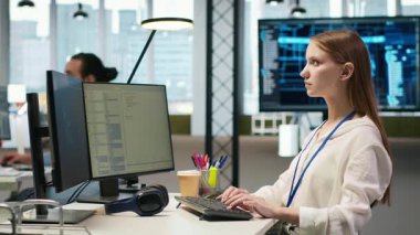 Başlangıç ofisinde bilgisayar kullanarak yapay zeka dili model yardımı alan kadın teknisyen kodlaması. Stajyer bilgisayar kullanıyor, yapay zeka LLM yardımcı önerilerini kod düzenleyiciye entegre ediyor, kamera A