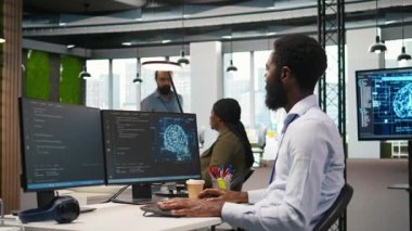 Bilgisayar bilimcisi yapay zekayı performansı ve tahminleri optimize etmek için kullanıyor. Ofis eğitim makinesinde çalışan Afrikalı Amerikalı işçi bilgisayar, kamera A kullanarak modeller öğreniyor.