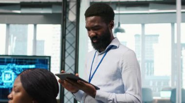 Ofis arkadaşlarının yanındaki teknisyen yazılım uygulamaları geliştiriyor, yapay zeka otomasyonunu entegre ediyor. İş yerindeki geliştiricilerin yanındaki Afrikalı Amerikalı adam hata ayıklama uygulamaları, kamera A