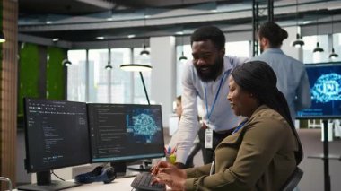 Bilgisayarda yapay zekayı performansı optimize etmek için kullanırken masalarda eğlenceli sohbetler yapan mutlu mühendisler. Ofisteki neşeli iş arkadaşları sohbet ediyor, PC, kamera A kullanarak derin öğrenim modelleri eğitiyorlar.