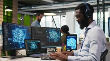 Ofisteki bilgisayar bilimcisi yapay zeka öğrenme sistemlerini iş akışlarını düzene sokacak şekilde entegre ediyor, kulaklık takıyor. Afrikalı Amerikalı adam cihazlar, dinleme müziği ve kamera A üzerinde yapay zeka kullanıyor.