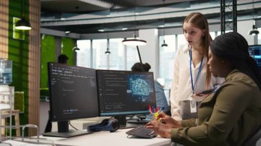 Yönetici, genç teknisyene yapay zeka kullanarak yazılımı nasıl geliştireceğini ve kodu nasıl optimize edeceğini öğretiyor. Takım lideri, başkanlık koltuğunda intörnlere suni zekanın darboğazları ve kamera A 'yı nasıl çözeceğini gösteriyor.