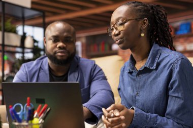 Bir iş fikrini paylaşmak için kanepeye oturan Afrikalı Amerikalı çift, modern teknoloji ve araçları trendleri analiz etmek ve başarıyı artırmak için kullanıyor. Bağımsızlar iş akışını verimli bir şekilde geliştiriyor.