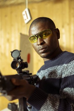 Antrenman yapan kişinin portresi, düzgün tüfek tutma adabı öğrenmesi, güvenlik gözlüğü takması. Atış poligonunda silahlı bir adam yaralanmayı önlemek için koruyucu giysi giyiyor.