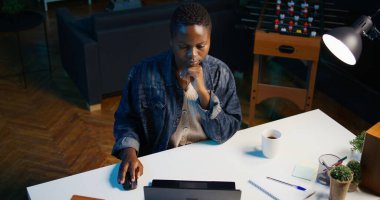 Oturma odasındaki kadın iş ortaklarından gelen e-postaları cevaplamak ve kahve içmek için dizüstü bilgisayar kullanıyor. Freelancer sıcak içecekten ve klavyede daktilo yazmaktan hoşlanıyor, kamera B