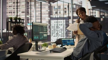 Siyahi erkek CEO sırt ağrısıyla uğraşıyor ve kaslarını masada geriyor, yanlış bir duruşla oturuyor ve düzeltmeye çalışıyor. Genel müdür veri analiziyle çalışıyor. Kamera B.