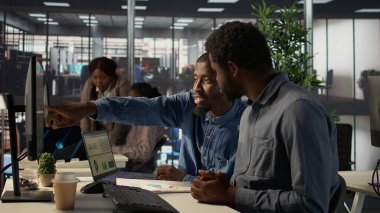 Afrikalı Amerikan takımı aylık gelir dengesini bilgisayarda inceliyor, verimli yatırımları sağlamak için finansal operasyonlarda bir sonraki adımları planlıyor. İşçiler performans ölçümlerini gözden geçiriyorlar. Kamera B.