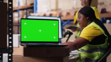 Personel veri girişi, envanter izleme motifleri ve görsel veya barkod yazıcı arayüzleri için depo odasındaki krom anahtar monitörünü gözden geçirir. Lojistik işçisi kargoyu ön planda paketler. Kamera B.