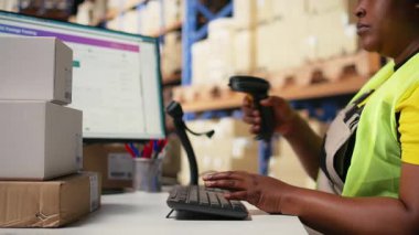 Afro-Amerikan personeli, dağıtım merkezindeki ambalaj görevlerinden sonra barkod sevkiyat etiketlerini kaydetmek için tarayıcı kullanarak etiketleri tarıyor. Depo odası. Kamera A.