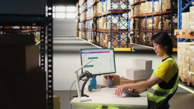 Asyalı depo işçisi teslimat işlemleri için takip numaralarını kaydediyor, teslimat işlemi için kutulara başvuruyor, paket izleme yazılımının sevkiyat detaylarını kaydediyor. Tatmin merkezi. Kamera A.