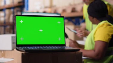 Lojistik çalışanı bilgisayarda izole edilmiş modellerin yanında paketler düzenliyor, sipariş izleme araçları yerleştiriyor ve etiketleme sistemleri yerleştiriyor. Personel üyesi, iş envanterini analiz ediyor. Kamera B.