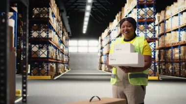 Siyahi bir kadın, raflarla dolu büyük bir iş deposundaki paketleri kontrol ederek siparişleri tamamlama sürecini yönetiyor. Perakende e-ticaret ekspres teslimat operasyonlarını çalışanlar denetliyor. Kamera A.