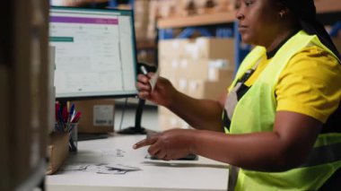 Siyah depo çalışanı etiketleme ve paketleme işlerini yönetir, basılı hava yolu faturalarını paketlere takip numaraları etiketleri ile uygular. Depoda yüksek çözünürlüklü kadın var. Kamera B.