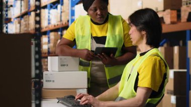 Depo çalışanları emirleri işliyor ve paketleri birlikte hazırlıyorlar, endüstriyel lojistik merkezinde perakende dağıtımı yapıyorlar. Depo raflarıyla çevrili yüksek çözünürlüklü yelek giyen takım. Kamera B.