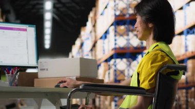 Tekerlekli sandalyedeki Asyalı adam talimatları işleme koyuyor ve kutuların dağıtım merkezindeki dağıtım için hazırlanıyor. Ticaret lojistik tesisinde yelek giyiyor. Hızlı teslimat. Kamera B.