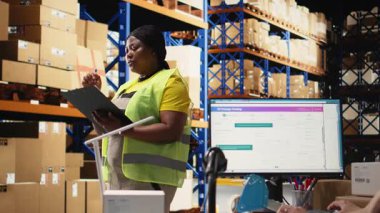 Siyah kadın işçi, envanter kontrolü için dosyalardaki yanlış etiketleri doğruluyor, raflardaki paketleri sayıyor ve depoya hızlı teslimat sağlıyor. E-ticaret havayolu faturaları. Kamera A.