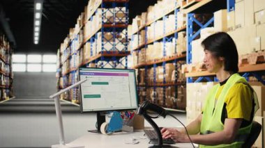 Asyalı bir çalışan, sanayi deposunda hava yolu faturalarını kaydediyor, paket izleme yazılımının sevkiyat detayları için barkod taraması yapıyor. Tatmin merkezi envanter takibi. Kamera A.