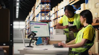 Depo çalışanları emirleri işliyor ve paketleri birlikte hazırlıyorlar, endüstriyel lojistik merkezinde perakende dağıtımı yapıyorlar. Depo raflarıyla çevrili yüksek çözünürlüklü yelek giyen takım. Kamera A.