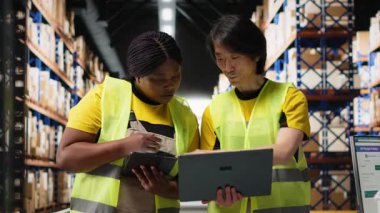 Afro-Amerikan ve Asyalı insanlar online siparişleri ve havayolu faturalarını yönetiyor, ürünleri paketlemeden önce envanteri kontrol ediyorlar. Büyük ticari perakende operasyonları. Kamera B.