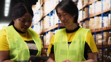 Çeşitli çalışanlar, dağıtım için sipariş detaylarını denetliyor dijital stok envanterlerini ve endüstriyel raflardaki kargo paletlerini kontrol ediyor. Büyük ölçekli hızlı teslimat. Kamera B.