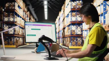 Asyalı erkek işçi sevkiyat etiketlerini ve dağıtım merkezindeki takip numaralarını tarıyor, tatmin merkezinde sipariş yönetimini garantiliyor. Ulaşım detayları için tarayıcı kullanıyor. Kamera A.