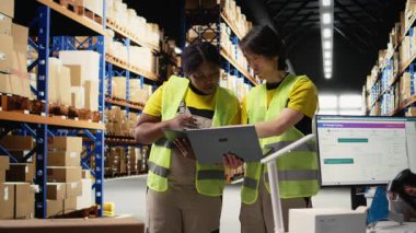 Endüstriyel depodan gelen raflı kargo sevkiyatını takip eden çeşitli işçiler, tabletteki paket durumları için takip yazılımlarıyla ilgileniyorlar. Çelik yelek personeli. Kamera A.