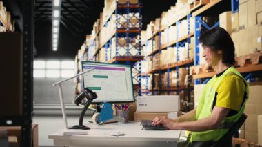 Endüstriyel depo alanında büyük bir depo rafının yanında çelik yelek giyen iki meslektaşım var. Asyalı adam bilgisayarda sevkiyat detaylarını yazıyor. Kamera A.