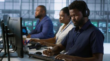 Klavyede veri merkezi yönetimi, donanımı yapılandırarak şirket ağ altyapısını koruyor. Sunucu merkezindeki Afrikalı Amerikalı işçi optimal sistem performansını garantiliyor, kamera A