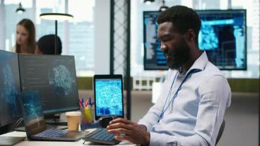 Ofis masasındaki sistem yöneticisi yapay zeka kullanarak yazılım geliştiriyor, müzik dinliyor. Bilgisayar üzerinde çalışan ses kulaklığı takan bilişim uzmanı, yapay zekayla hata ayıklama uygulamaları, kamera A