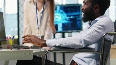 Felç olmuş genç mühendis ve iş arkadaşı ofiste beyin fırtınası yapıyor, yapay zeka ölçümlerini inceliyor. Tekerlekli sandalyedeki küçük dev ve meslektaşı konuşuyor, sinirsel ağları PC, kamera A kullanarak ayarlıyorlar.