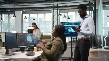 Ofis arkadaşlarının yanındaki teknisyen yazılım uygulamaları geliştiriyor, yapay zeka otomasyonunu entegre ediyor. İş yerindeki geliştiricilerin yanındaki Afrikalı Amerikalı adam hata ayıklama uygulamaları, kamera A