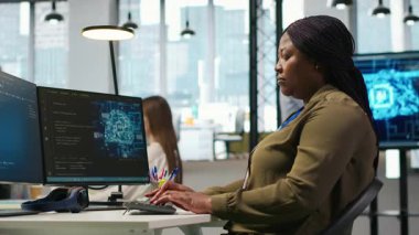 Başlangıç ofisindeki bilgisayar bilimci yapay zeka sistem ölçümlerini gözden geçiriyor, performans gösterge panellerini izliyor. Afrika kökenli Amerikalı bir kadın, bilgisayar ve kamera A 'daki araçları kullanarak sinirsel ağları ayarlıyor.
