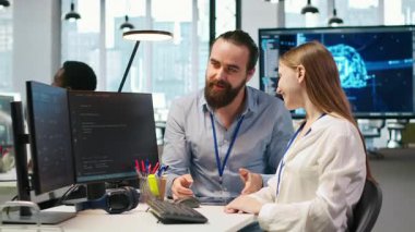 Arkadaş canlısı ekip lideri, yazılım sorunlarını çözmek ve sistem istikrarını geliştirmek için genç mühendis yapay zeka algoritmalarını kodlamaya yardım ediyor. Yardımcı yönetici, teknoloji firması ofisinde gülümseyen stajyere yardımcı oluyor, kamera A