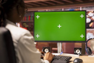 Daire ofisindeki serbest çalışan, iş için yeşil ekran bilgisayar ekranını kullanıyor. Çevrimiçi iş yapmak için krom anahtar bilgisayar monitörü kullanarak evdeki uzak çalışanın görüntüsünü kapat