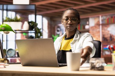 Sabahları ofiste kahve içen, internete girip bilgi arayan bir kadın. Afrika kökenli Amerikalı tele-işçi iş vardiyasına sıcak içecekle başlıyor, iş yapmaya hazırlanıyor.