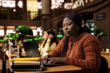 Kadın eğitimci kütüphanede eğitim materyallerini ve kaynaklarını hazırlıyor, uzmanlığını akademisyenlere danışmanlık yapmak ve genç zihinler için üretken bir akademik atmosfer yaratmak için kullanıyor..