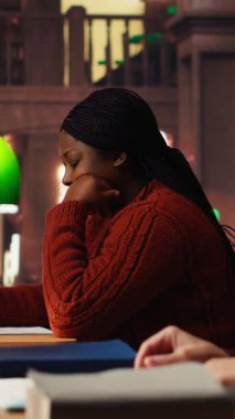 Yeşil bir lamba altında, basılı bir kütüphanedeki yazılı derslerde, okuma ve fosforlu kalem kullanan dikey video erişkin kadın, belgeleri incelemeye odaklandı. Önemli ders fikirlerini ezberlemek. Kamera B.