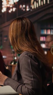 Kütüphanede, akademik materyal ve kitaplarla çevrili çalışmalarına odaklanarak önemli sınav fikirlerini vurgulayan dikey video olgun kadın öğrenci. Strateji ezberlemesi çalış. Kamera A.