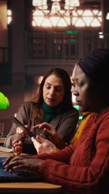 Akademik kütüphane kaynaklarından notlar alan ve arşivlenmiş materyalleri bir çalışma alanında inceleyen dikey video odaklı öğrenciler, olgun eğitim ve bilgi binasının adanmışlığını göstermektedir. Kamera.