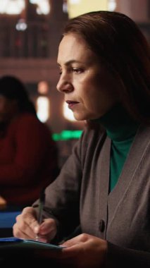 Üniversite kampüs kütüphanesindeki bir tez projesini araştıran dikey video erişkin kız öğrenci akademik başarı için ilham ve adanmışlık göstermektedir. Evrak işleriyle uğraşıyorum. Kamera A.