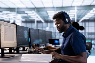 Sunucu odası programcısı müzik dinliyor, bilgisayardaki yüksek performanslı yapay zeka sistemlerini oluşturduktan sonra evraklara bakıyor. Veri merkezinde kulaklık takan bir mühendis yapay zeka belgelerini kontrol ediyor.