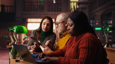 Akademik kütüphane kaynaklarından notlar alan ve bir çalışma alanındaki arşivlenmiş materyalleri inceleyen odaklanmış öğrenciler, olgun eğitim ve bilgi oluşturmanın adanmışlığını gösteriyor. Kamera B.