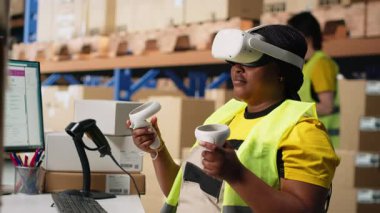 Afro-Amerikalı bir kadın siparişleri işlemek ve paket sevkiyatını yönetmek için sanal gerçeklik sisteminde çalışıyor, ücretsiz envanter kontrolü yapıyor. Sanal gerçeklik hızlı teslimatı garanti eder. Kamera B.