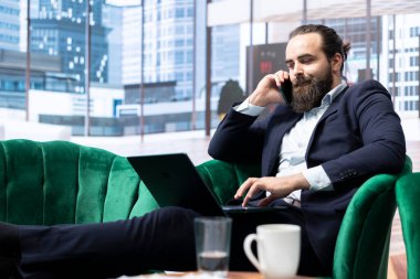 İşadamı, şirketinin varlıklarını korumak için bir sigortacıyla konuşuyor. Bilgisayarındaki önemli finansal güncellemeleri takip ediyor. Güvenlik danışmanına telefon var..