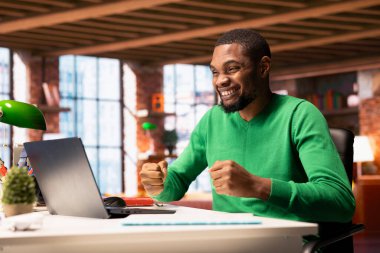 Memleketteki neşeli adamın yumruklarını mutlu bir şekilde sallaması, başarılardan mest olması. Heyecanlı bir Afrikalı Amerikalı, dizüstü bilgisayardaki iyi haber e-postalarını okuduktan sonra kutlama yapıyor.