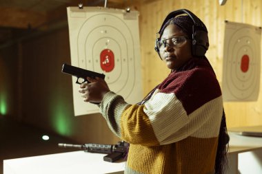 Atış poligonunda eğitim yapan, düzgün silah kullanmayı öğrenen bir kadının portresi. Afrikalı Amerikalı tabancayla alıştırma yapıyor, gözlük takıyor ve enkazın gözünüze girmesini engelliyor.