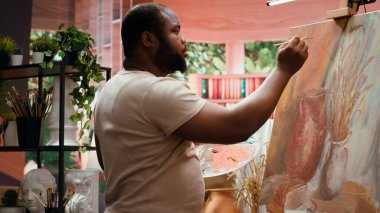 Odaklanmış bir adam fırça darbeleri desenli tuvale yeni bir rustik resim çiziyor sulu boyaları karıştırıyor ve bir başyapıt yaratmak için başvuruyor. Yaratılışı üzerinde çalışan genç bir erkek sanatçı. Kamera A.