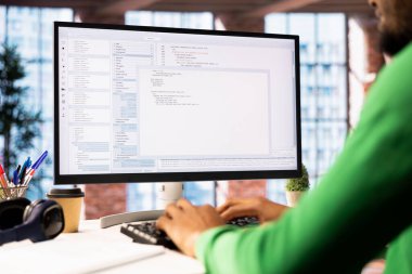 Ofisteki teknisyen UI 'ye bilgisayar monitöründe bakıyor, programlama kodunu yazıyor ve çalıştırıyor. IT çalışanının modern apartmanda kod yazma ve test etme uygulaması kullanarak yakın plan fotoğrafını çek.