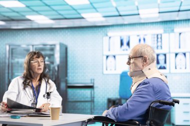 Kronik sakatlığı ve boyun yaralanması olan, boyun köpüğü tasması takan ve sağlık dolabında tekerlekli sandalye kullanan bir hekim. Engelli dayanışma bürosundaki sağlık görevlisi.