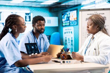 Doktorla sonuçları analiz eden, modern bir ofiste takım çalışması, profesyonel eğitim ve bakım yönetimi konularını vurgulayan bir grup önlük uzmanı. Tıbbi personel araştırma yapıyor..